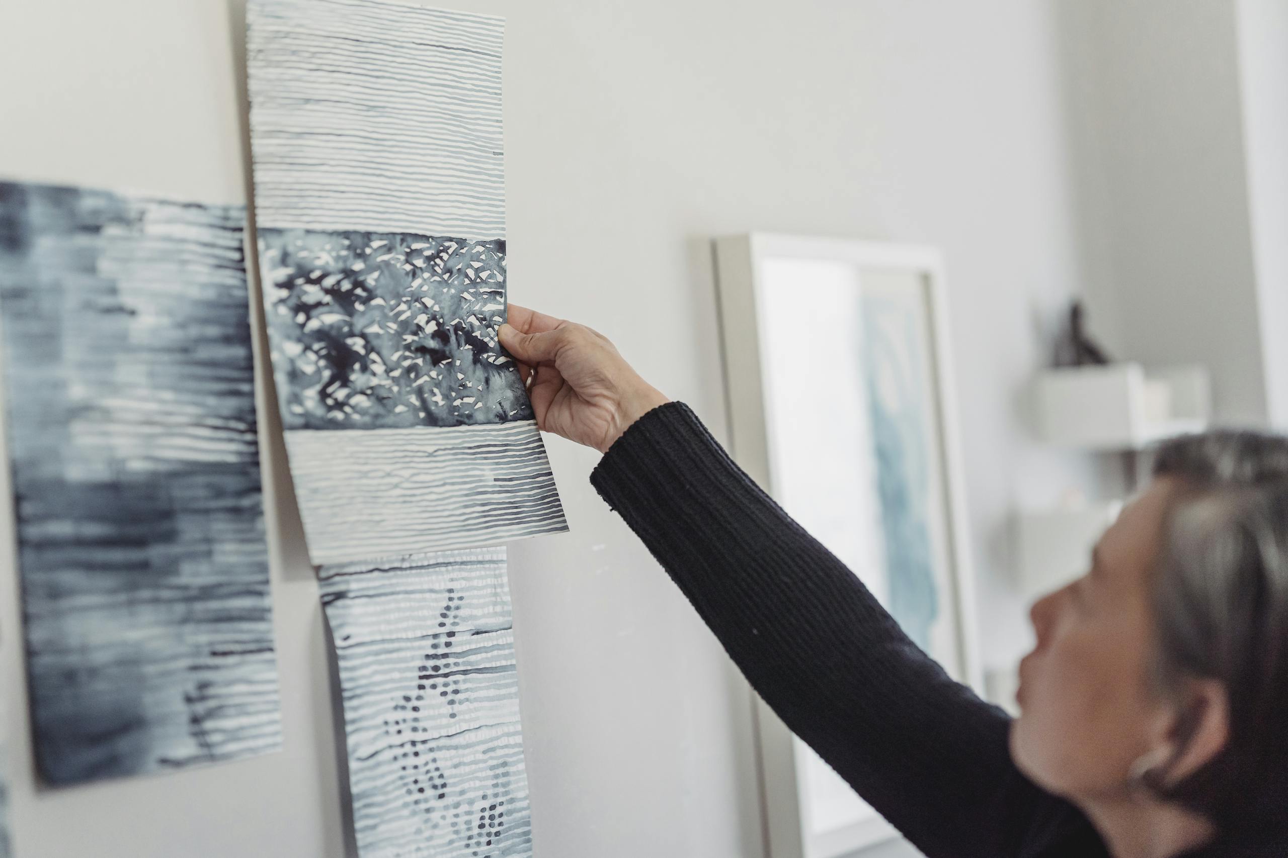 A woman arranges abstract paintings on an indoor gallery wall, focusing on creativity.