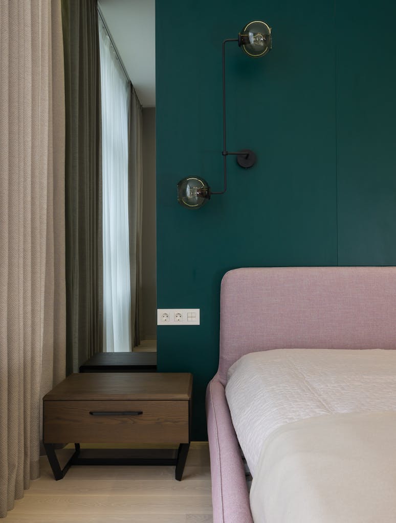 Details of interior of modern bedroom with mirror and lamps decorating wall near cozy bedroom and wooden nightstand