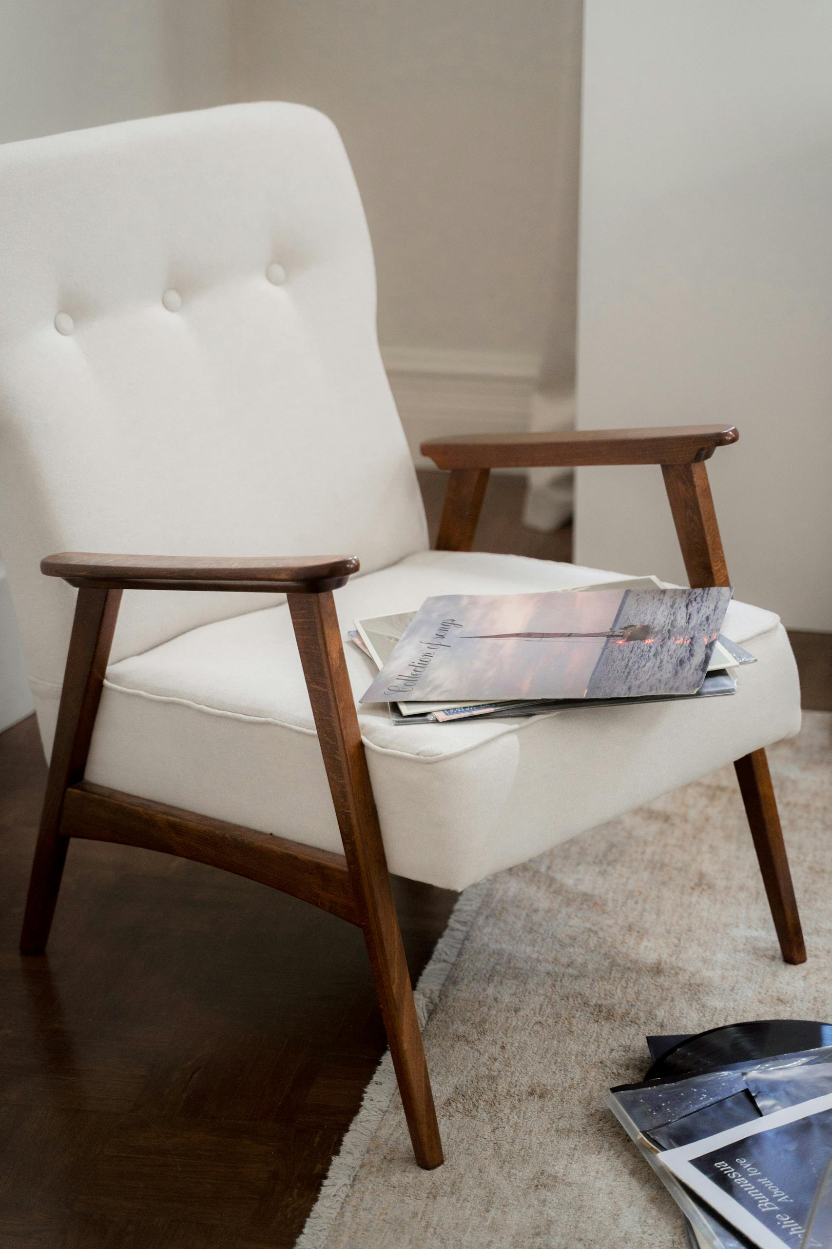 Elegant mid-century modern armchair with magazines on a plush carpet in a warm living room setting.