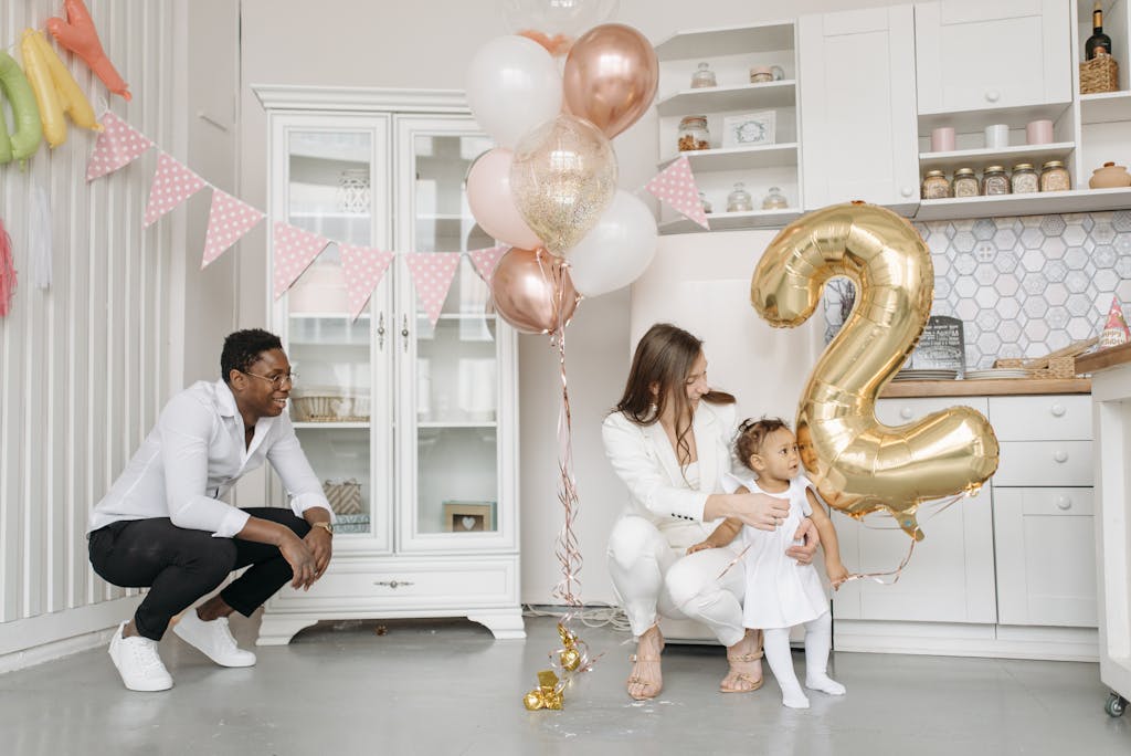 Family celebrating a child's second birthday in a decorated kitchen with balloons.