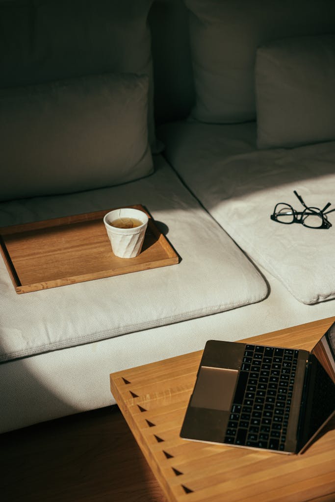 Modern home office corner with laptop, coffee, and glasses in warm lighting for productivity and comfort.